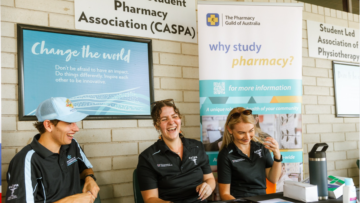 Three students from the UC Student Pharmacy Association behind a table at market day. 